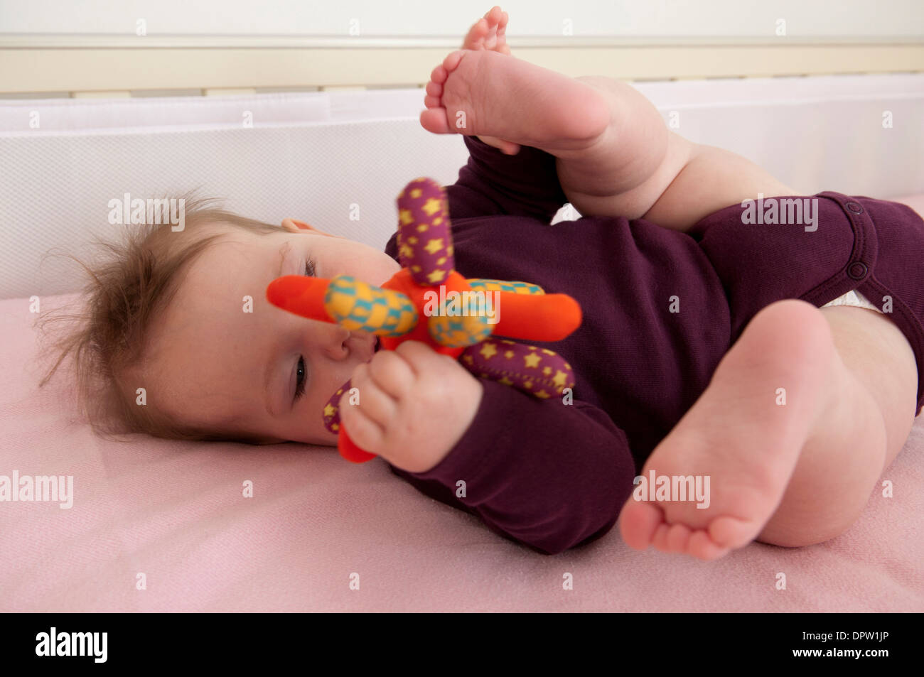 Babymädchen liegend in ihrem Bett und spielt mit einem Stofftier Stockfoto