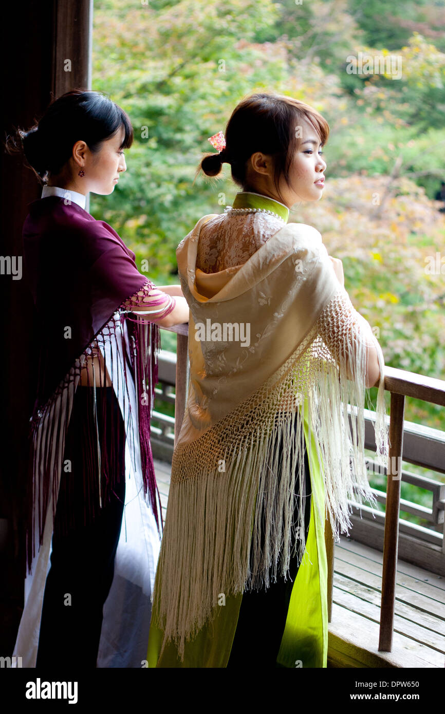 Zwei junge Frauen im traditionellen vietnamesischen Kleid mit Blick auf die Holzschiene am Teich. Stockfoto