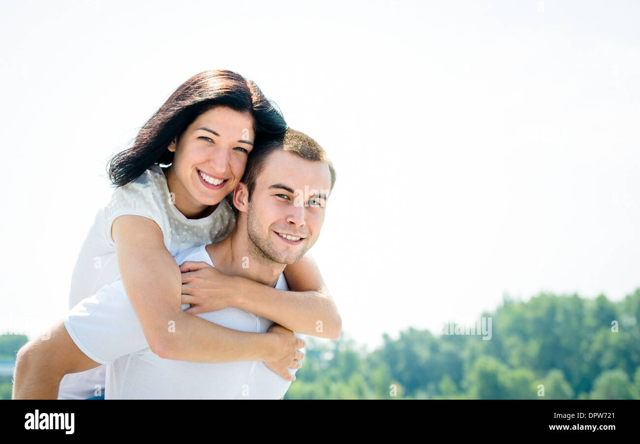 Glückliches junges Paar - lächelnde Frau Embbracing ihrem Freund um Hals Stockfoto