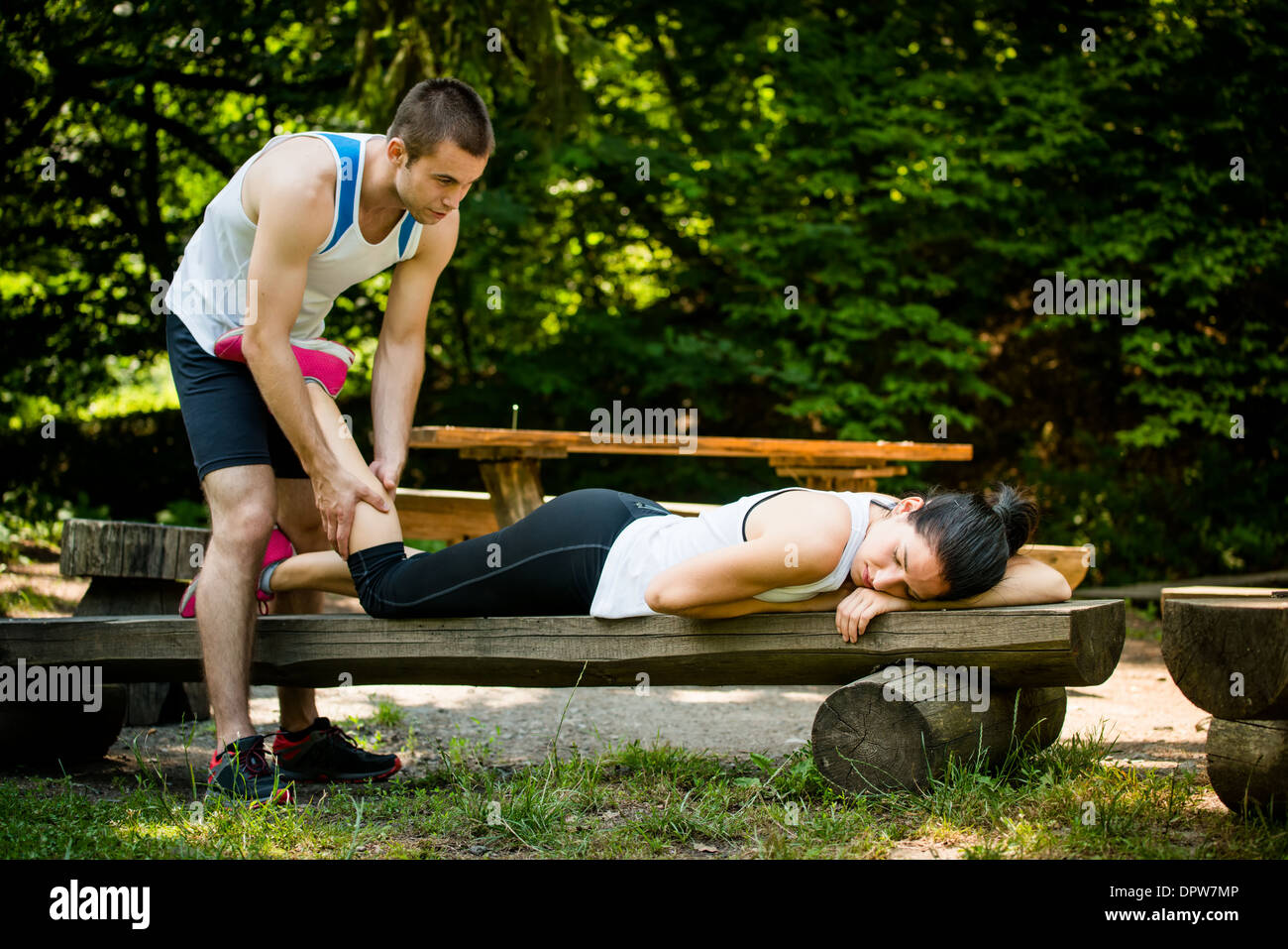 Mann gibt Massage des Kalbes zu seiner Freundin nach dem Sport Training - Frau liegt auf Bank Stockfoto