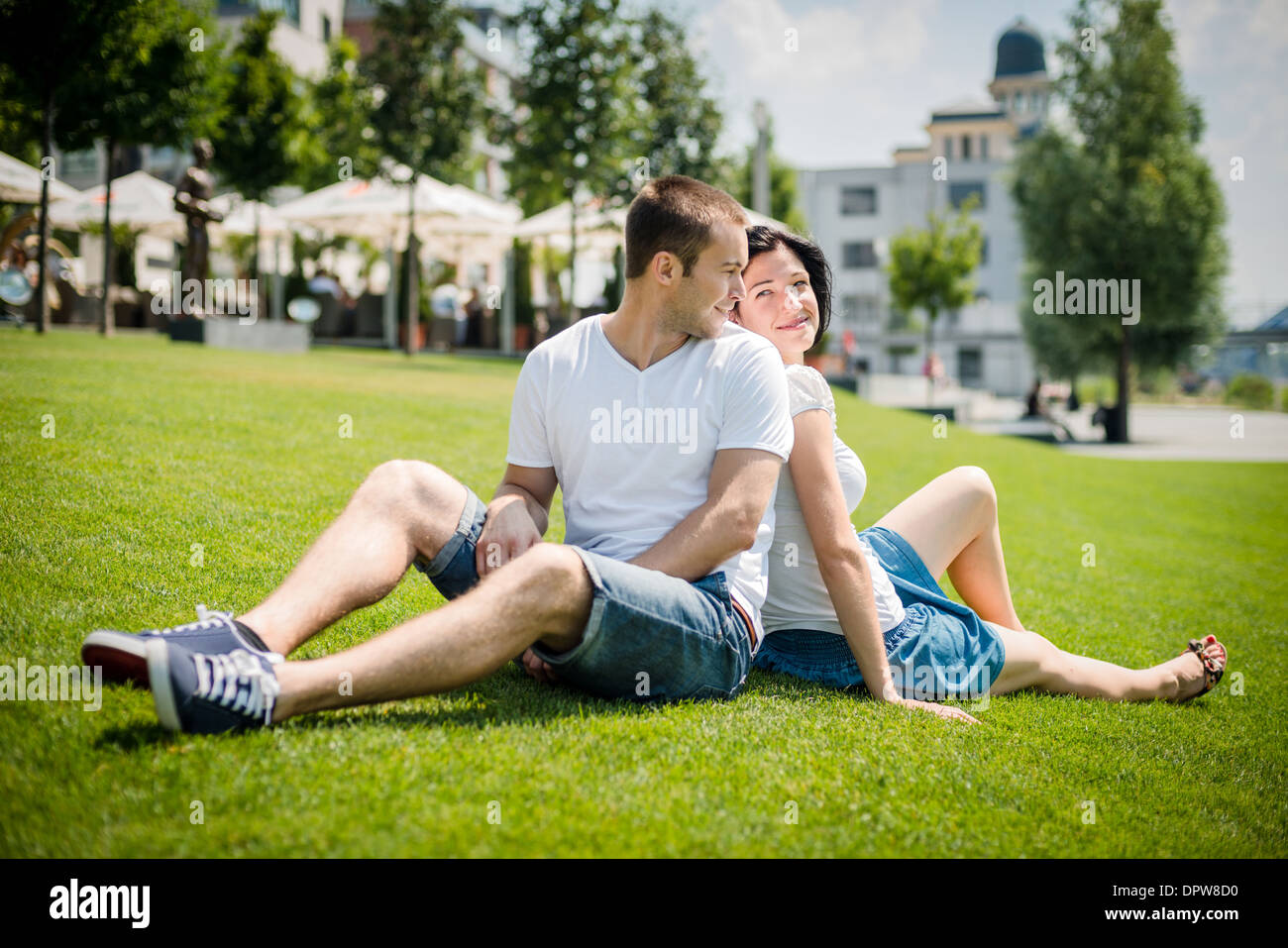 Junges Paar auf dem Rasen sitzen, mit Rücken gelehnt und lächelnd über die Schulter Stockfoto