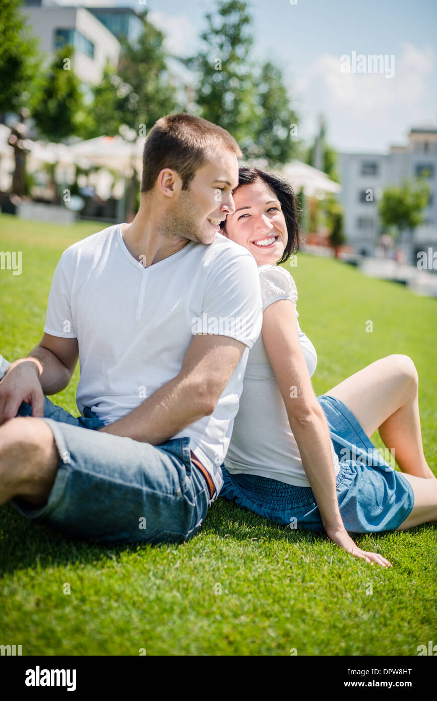 Junges Paar auf dem Rasen sitzen, mit Rücken gelehnt und lächelnd über die Schulter Stockfoto