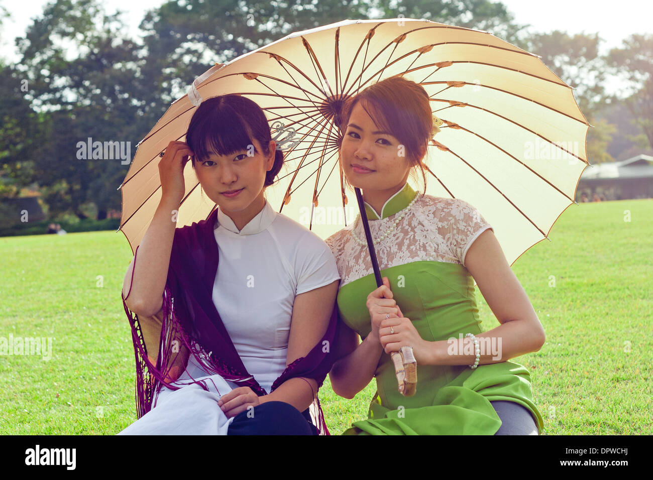 Junge Frauen halten Sonnenschirme in vietnamesischen Tracht lächelnd in die Kamera kniend Stockfoto