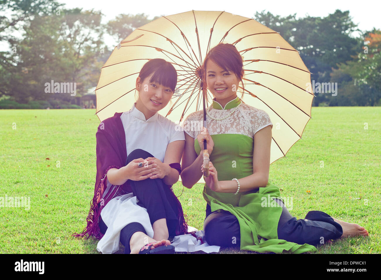 Junge Frauen halten Sonnenschirme in vietnamesischen Tracht lächelnd in die Kamera kniend Stockfoto