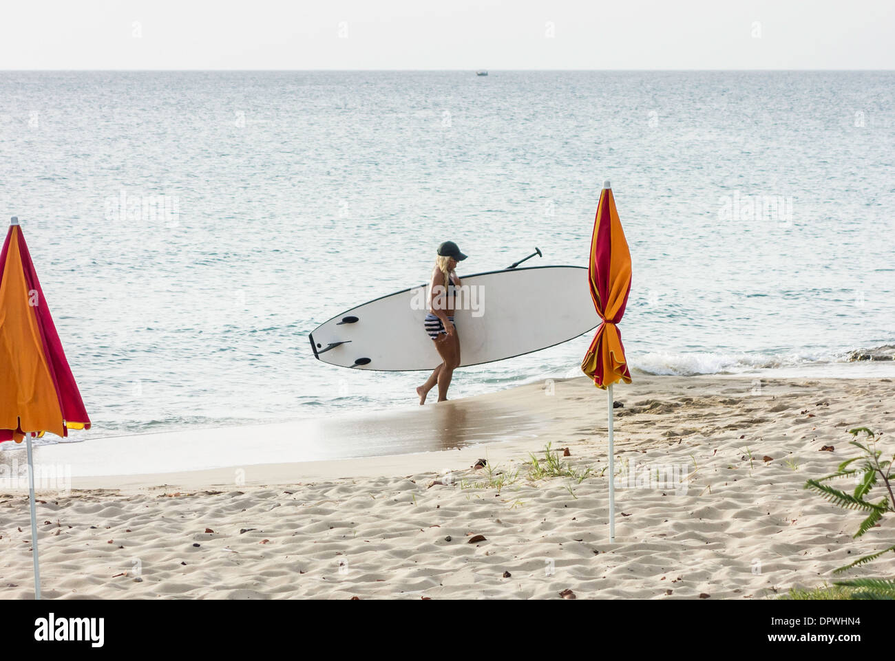Eine junge Frau in einem zweiteiligen Badeanzug trägt ihr Stand up Board aus der Karibischen Meer und auf den Strand paddeln. Stockfoto