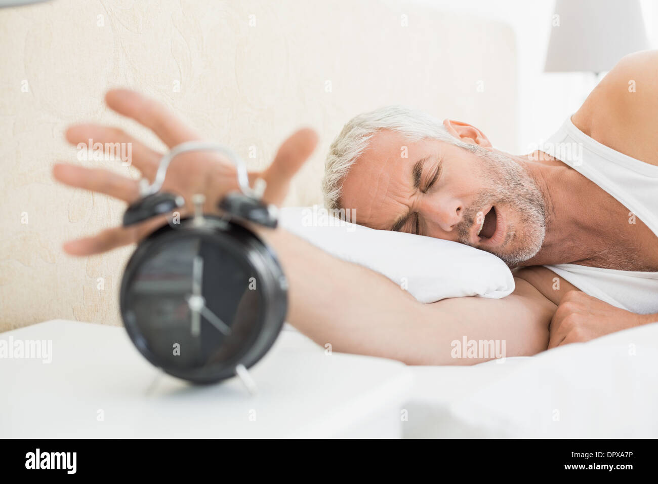 Verschlafene reifer Mann streckte Hand mit Wecker Stockfoto