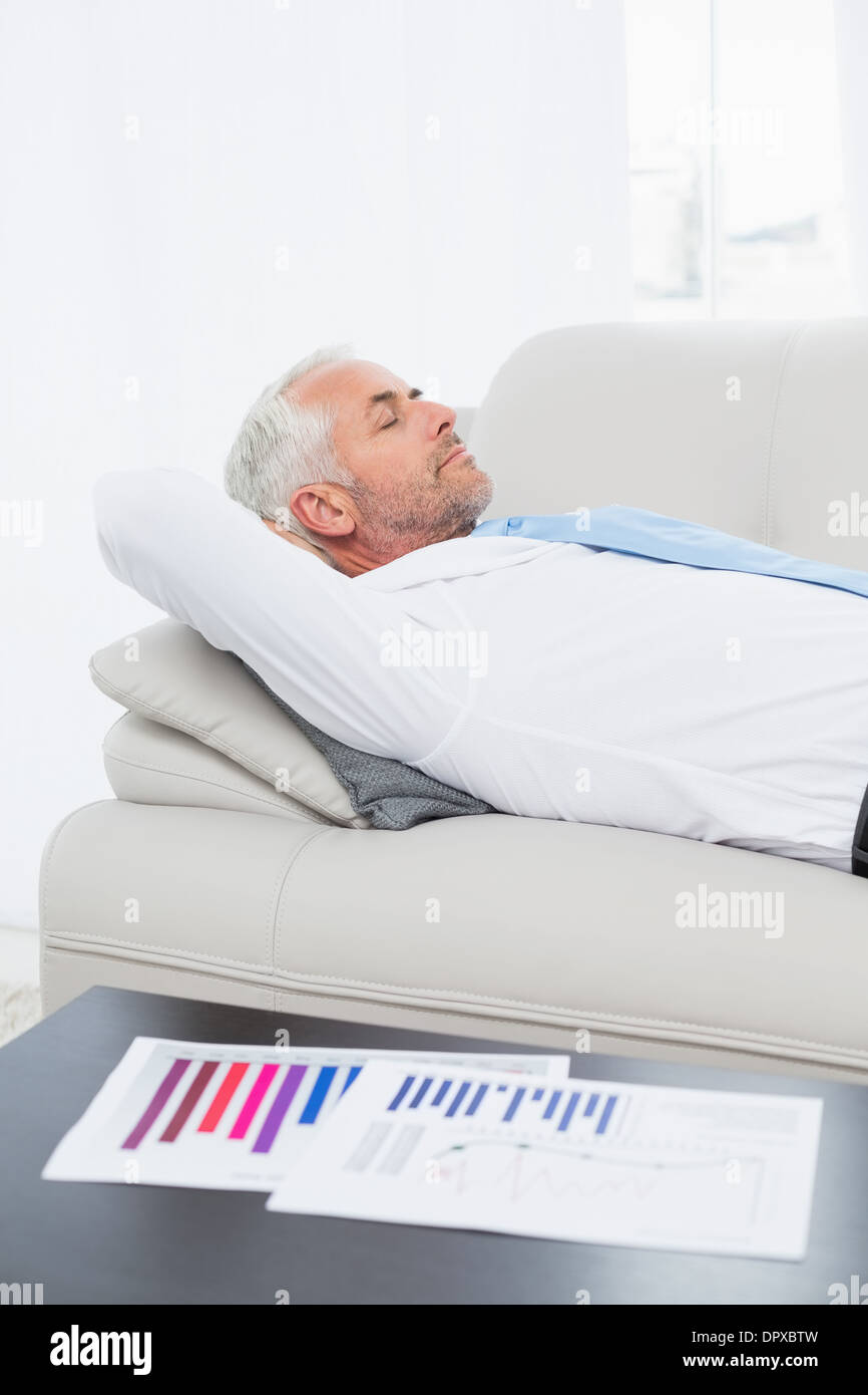 Geschäftsmann auf Sofa mit Grafiken auf Tisch im Wohnzimmer schlafen Stockfoto