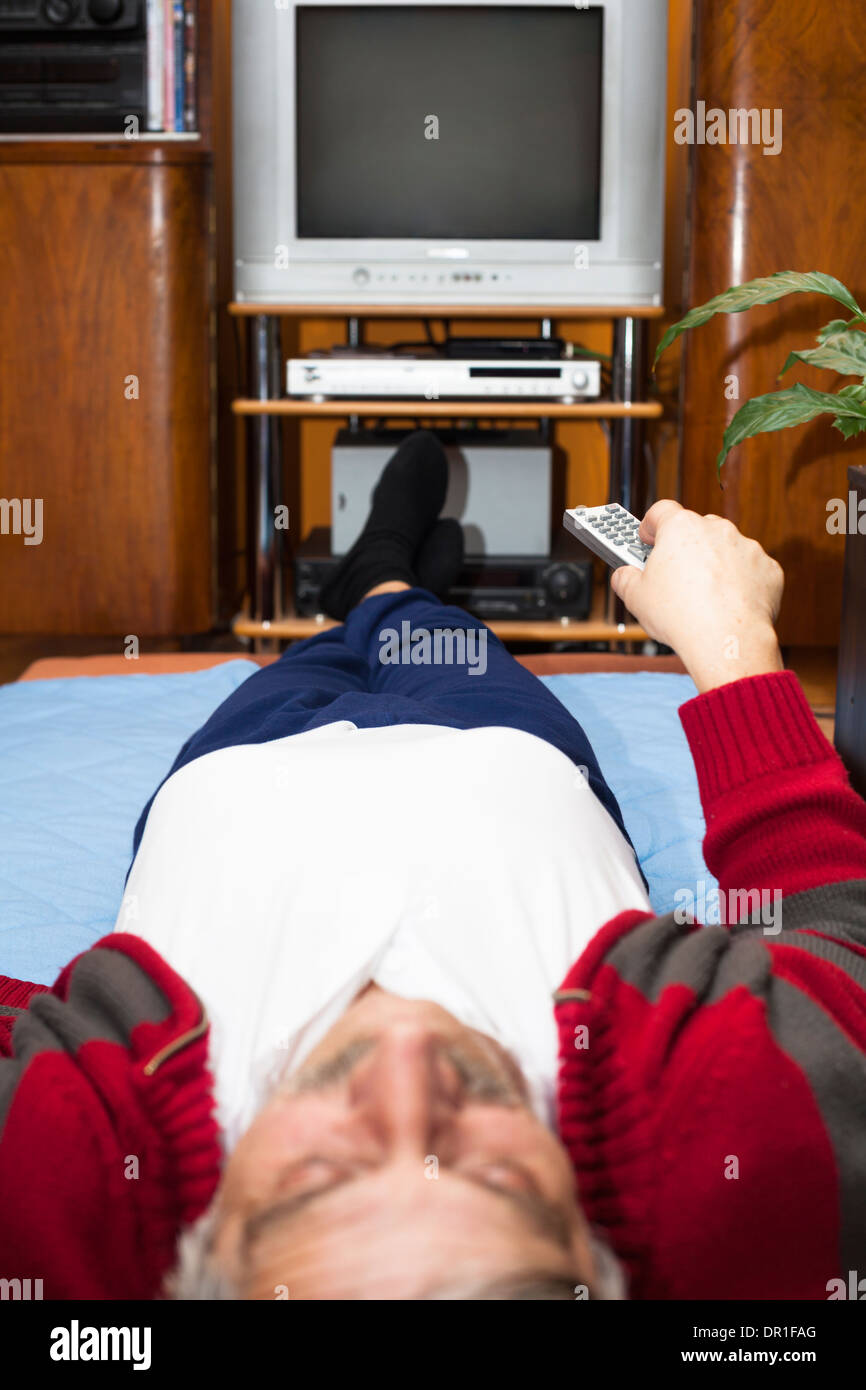 Älterer Mann mit Fernbedienung vor dem Fernseher zu Hause. Geringe Schärfentiefe mit Fokus auf Fernbedienung. Stockfoto