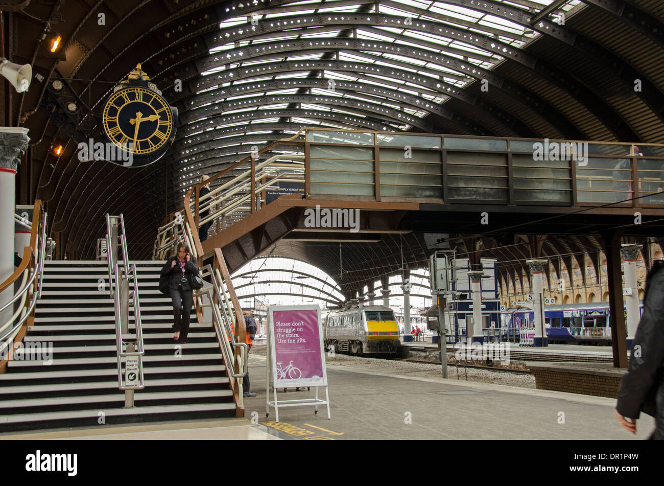 Innenraum der trainshed mit Eisen & Glas dach, stationäre Züge & Frau zu Fuß durch Plattform Uhr - Der Bahnhof York, North Yorkshire, England, Großbritannien Stockfoto