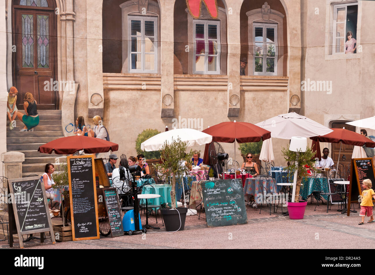 Menschen mit Mittagessen im Außenrestaurant mit Wandbild im Hintergrund, Montpellier, Hérault, Languedoc-Roussillon, Frankreich Stockfoto