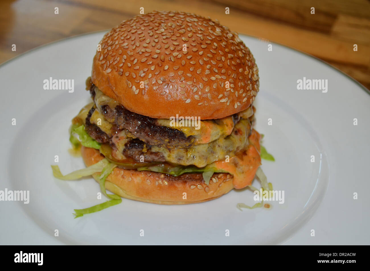 Double Cheeseburger mit Sesam Brötchen auf einem Porzellanteller serviert Stockfoto