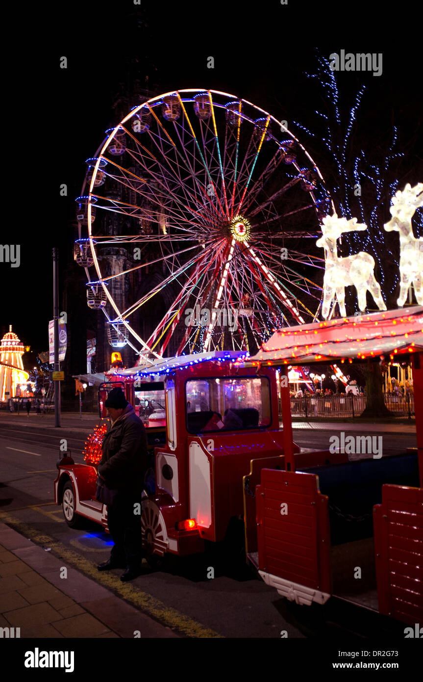 Zug auf der Princess Street im Winter Festival in Edinburgh, Schottland, Großbritannien. Das große Riesenrad leuchtet mit hellen Lichtern neben dem Weihnachtsmarkt Stockfoto