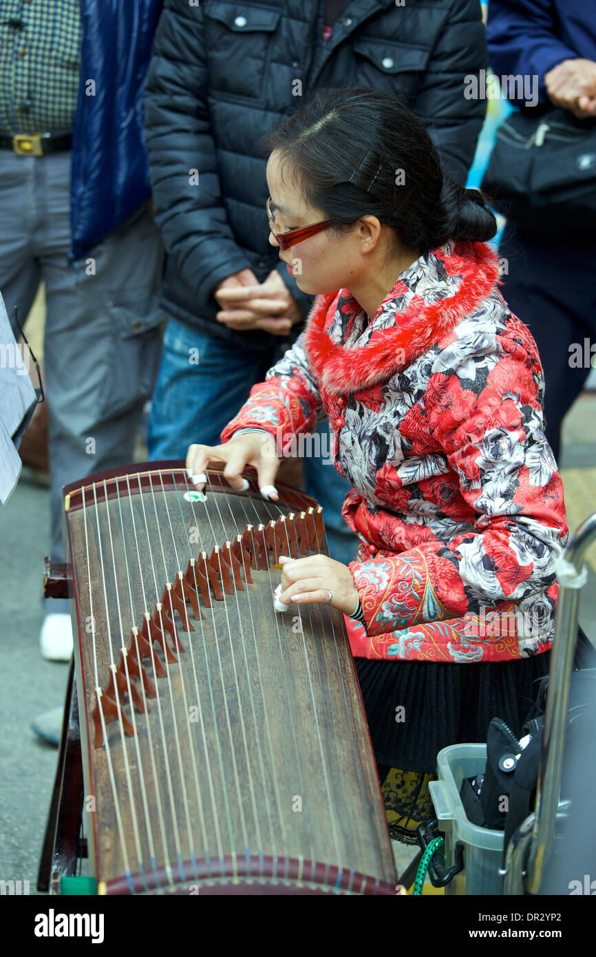 Junge orientalische Frau spielt eine chinesische Zither mit einer Masse in Mong Kok, Hong Kong. Stockfoto