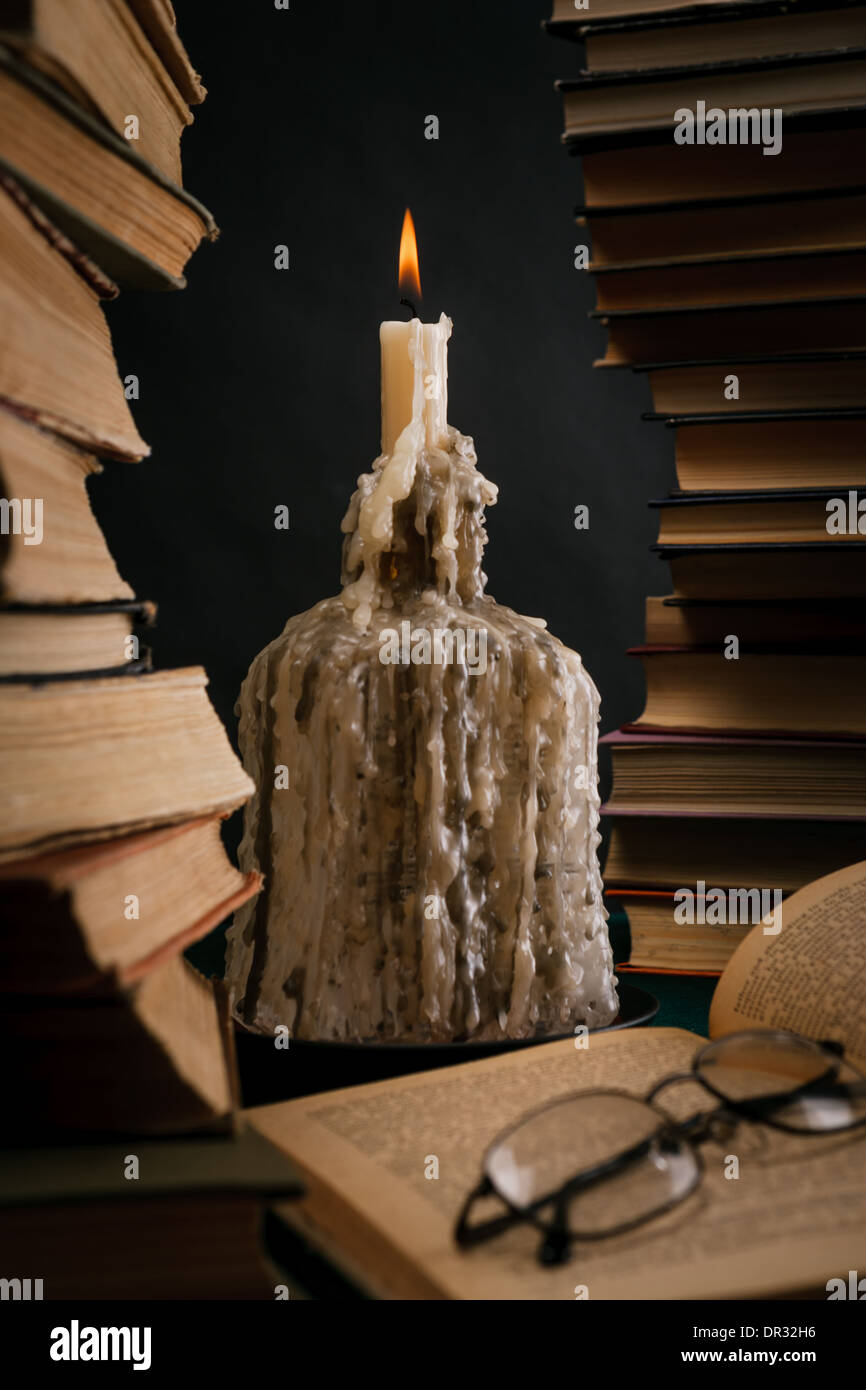 eine schmelzende Kerze in einer Flasche unter alten Büchern Stockfoto