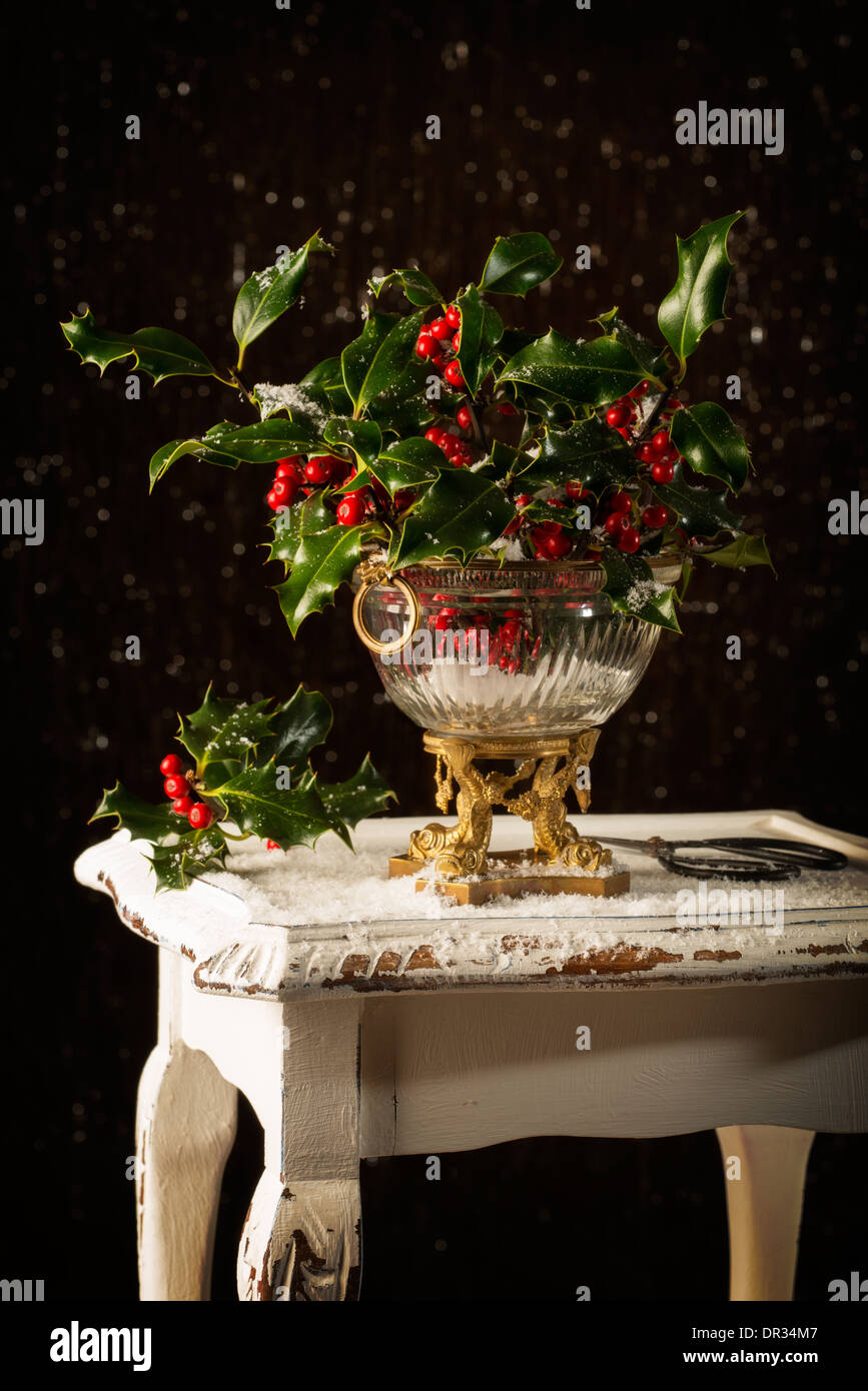 Christmas Holly und Beeren in eine Antike Glasvase auf rustikalen Tisch Stockfoto