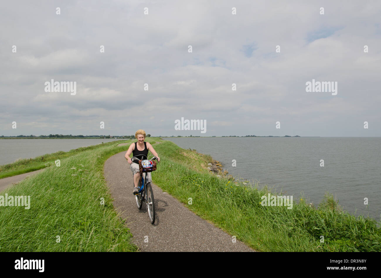 Eine Frau, Radfahren auf einem Polder Deich nördlich von Amsterdam. Stockfoto