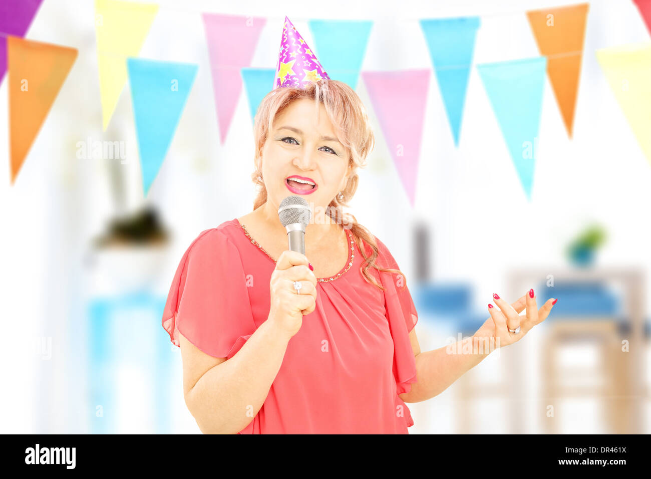 Reife Dame mit Party Hut singen am Mikrofon bei einer Geburtstagsparty Stockfoto
