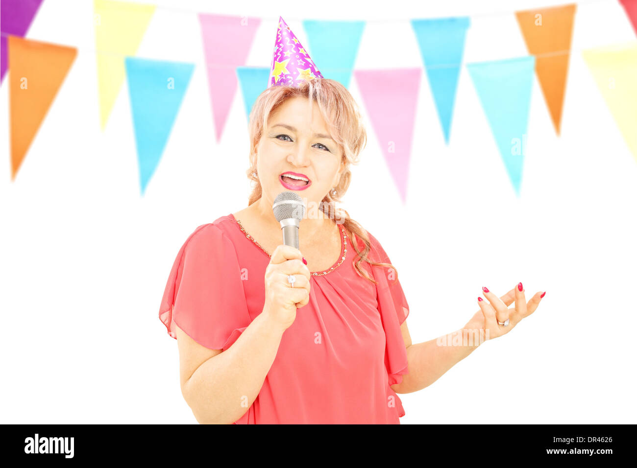 Reife Dame mit Party Hut singen am Mikrofon bei einer Geburtstagsparty Stockfoto
