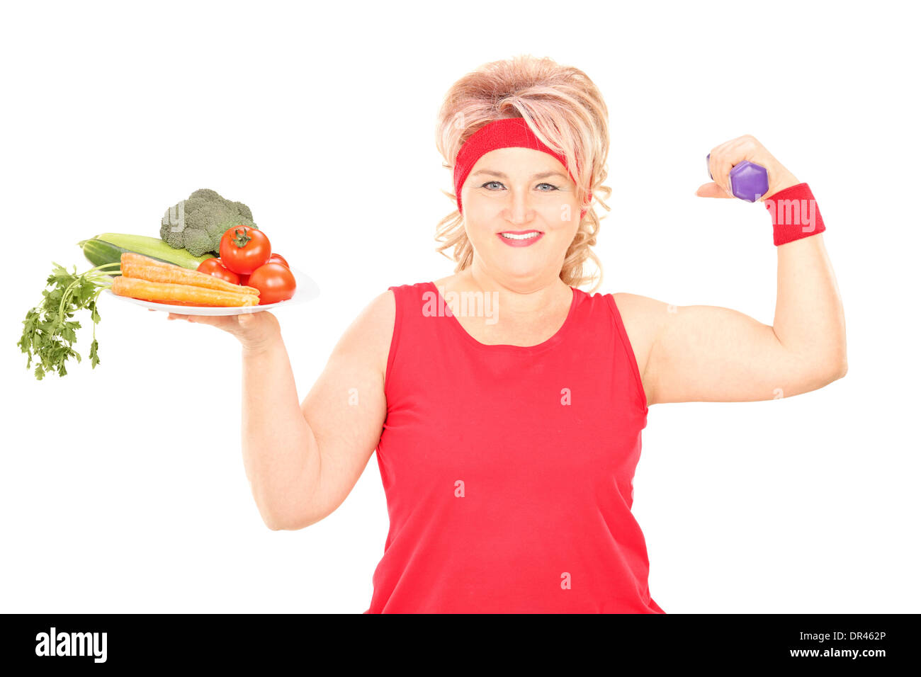 Reife Frau hält Teller mit Gemüse und eine Hantel Stockfoto