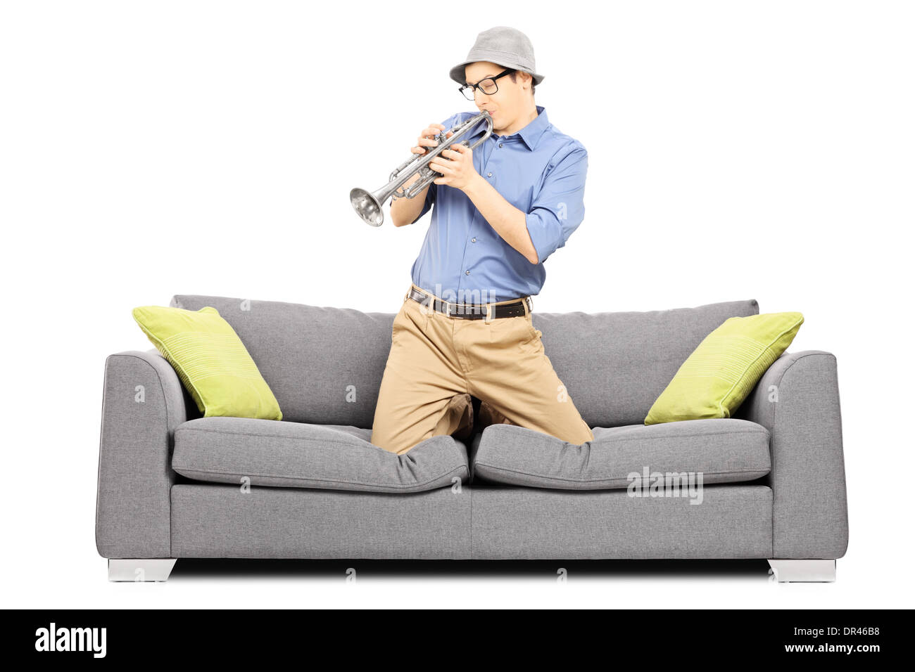 Junger Mann auf Sofa sitzen und an der Trompete bläst Stockfoto