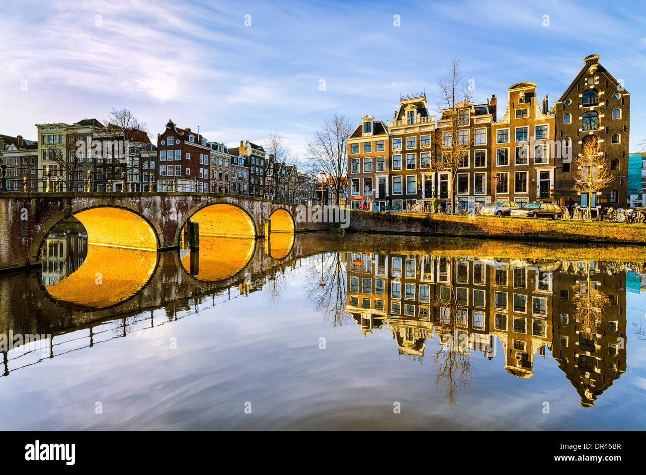 Sonnigen Morgen an einer Gracht in Amsterdam, Niederlande mit der Sonne, unter einer Bogenbrücke Stockfoto