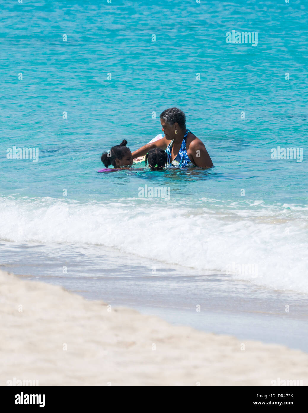 Eine afroamerikanische Frau kümmert sich um Ihre zwei Enkelinnen beim Schwimmen in der Karibik aus Sandcastle Strand in St. Croix, US Virgin Islands. Stockfoto