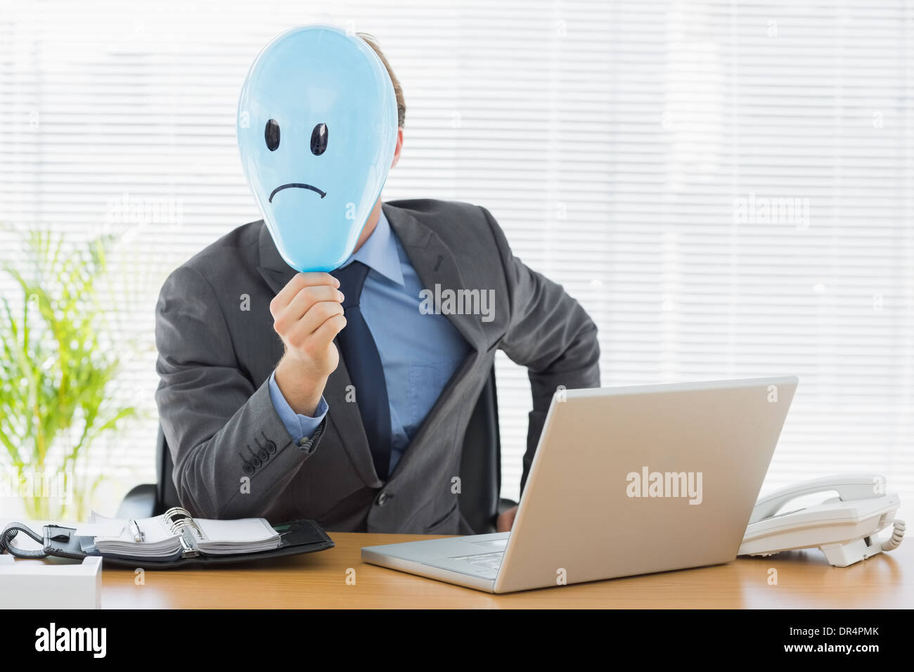 Geschäftsmann hält traurigen Smiley konfrontiert Ballon im Büro Stockfoto