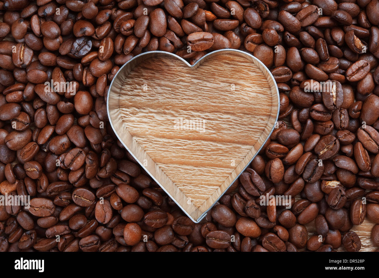 Kaffeebohnen als Hintergrund von gut gerösteten Kaffeebohnen mit Herz geformt Metallrahmen Stockfoto