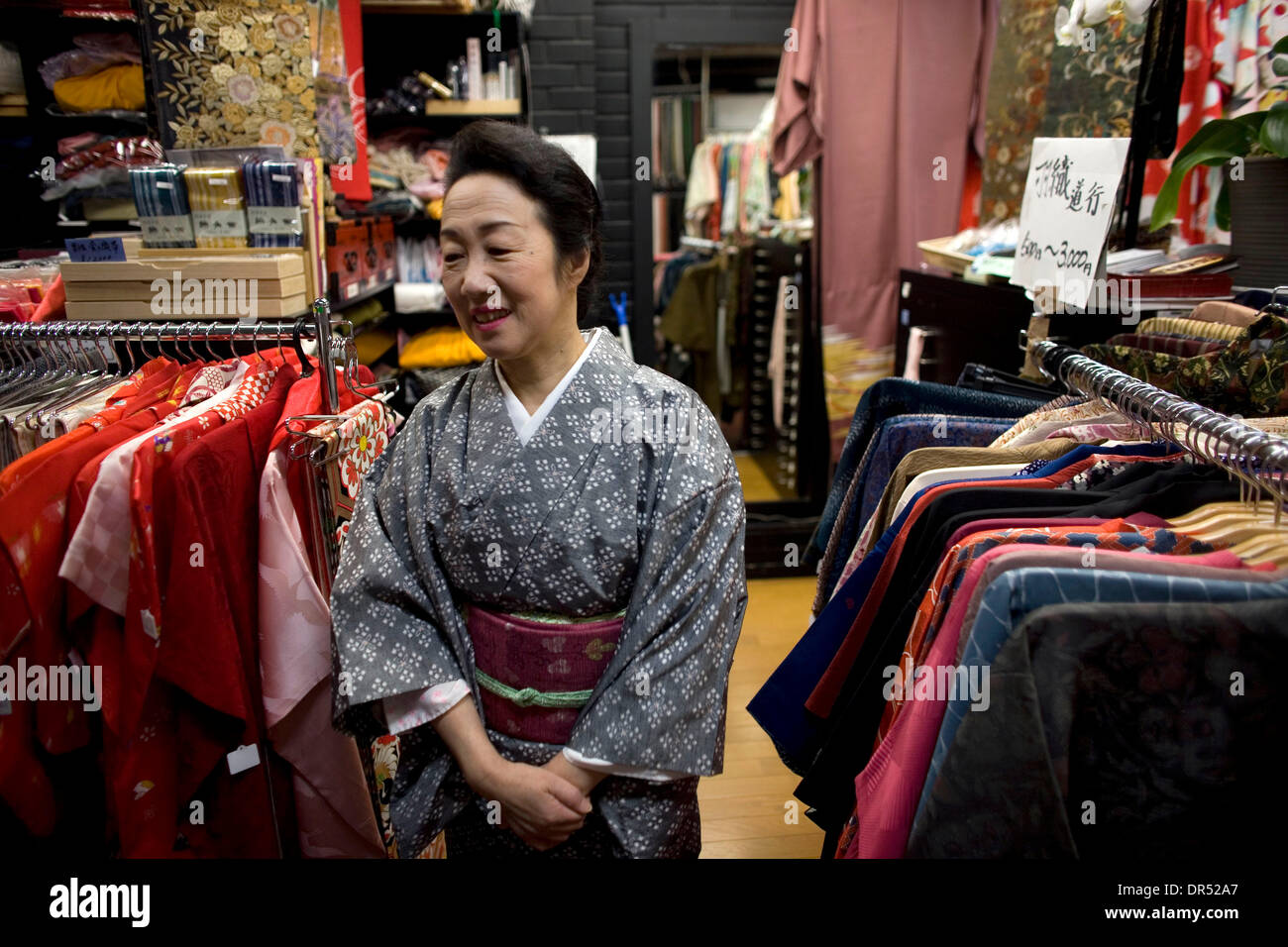 Apan - steht eine Frau unter Racks von üblichen Kleidung. Kimonos sind die traditionellen japanischen Kleiderordnung. Allerdings sind sie meist von älteren Frauen getragen. Jüngere Erwachsene bevorzugen die moderne Mode-Stil. Stockfoto