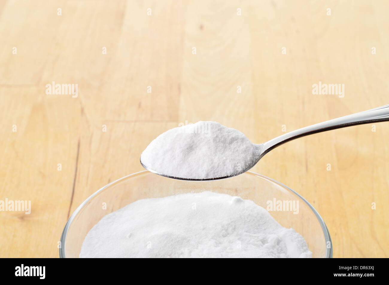 Nahaufnahme von Backpulver auf Löffel vor Hintergrund des Glases des Wassers auf Holztisch. Natron. Stockfoto