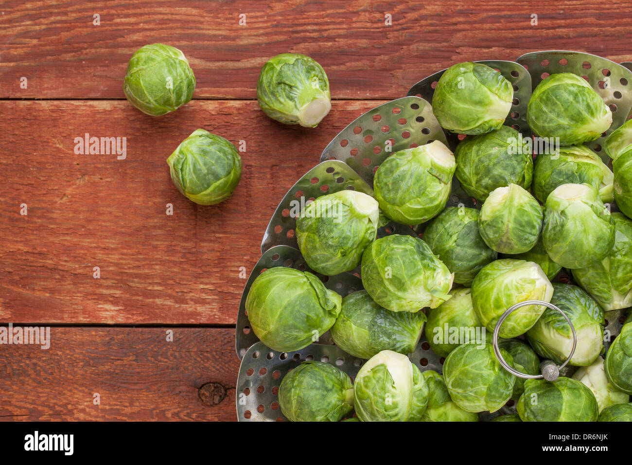 frischer Rosenkohl in Metall Dämpfeinsatz auf roten rustikalen Holztisch Stockfoto