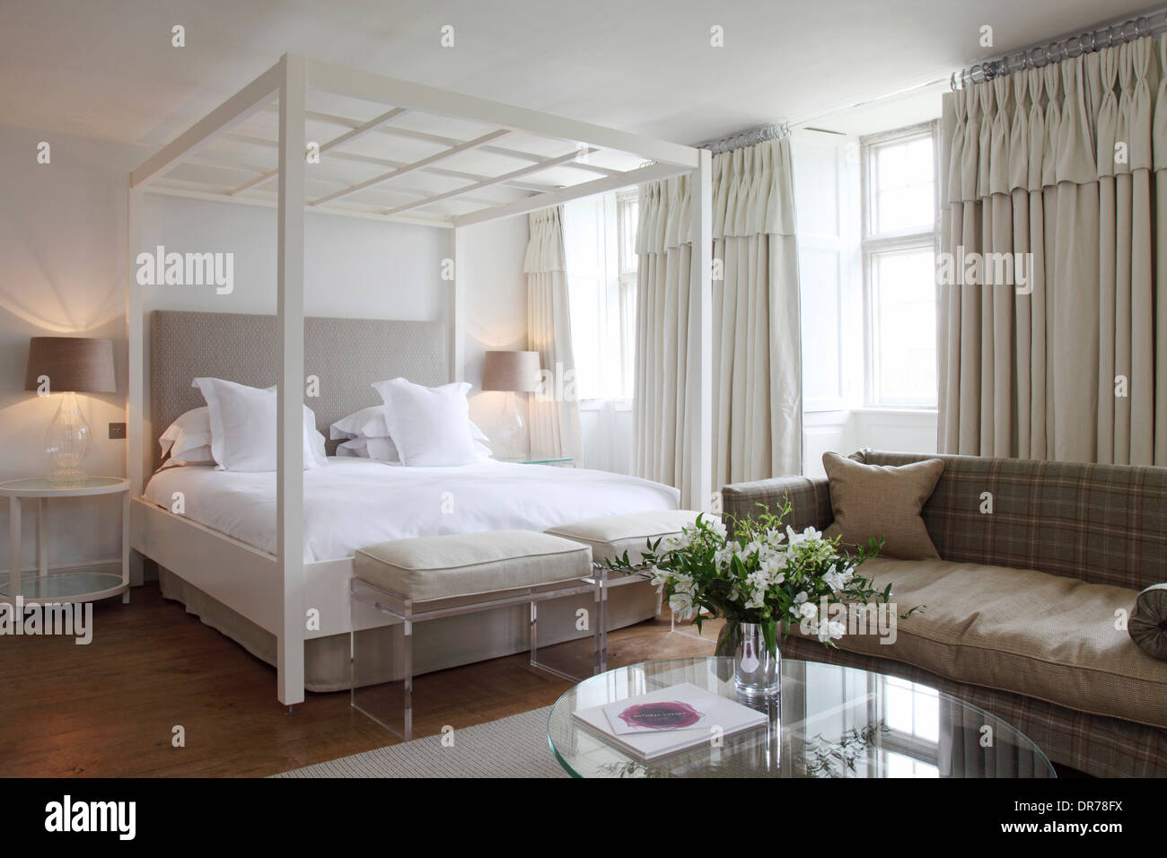Weißes Himmelbett in Hotelsuite mit Blumen auf Glastisch Barnsley House Hotel, Barnsley, Cotswolds Stockfoto