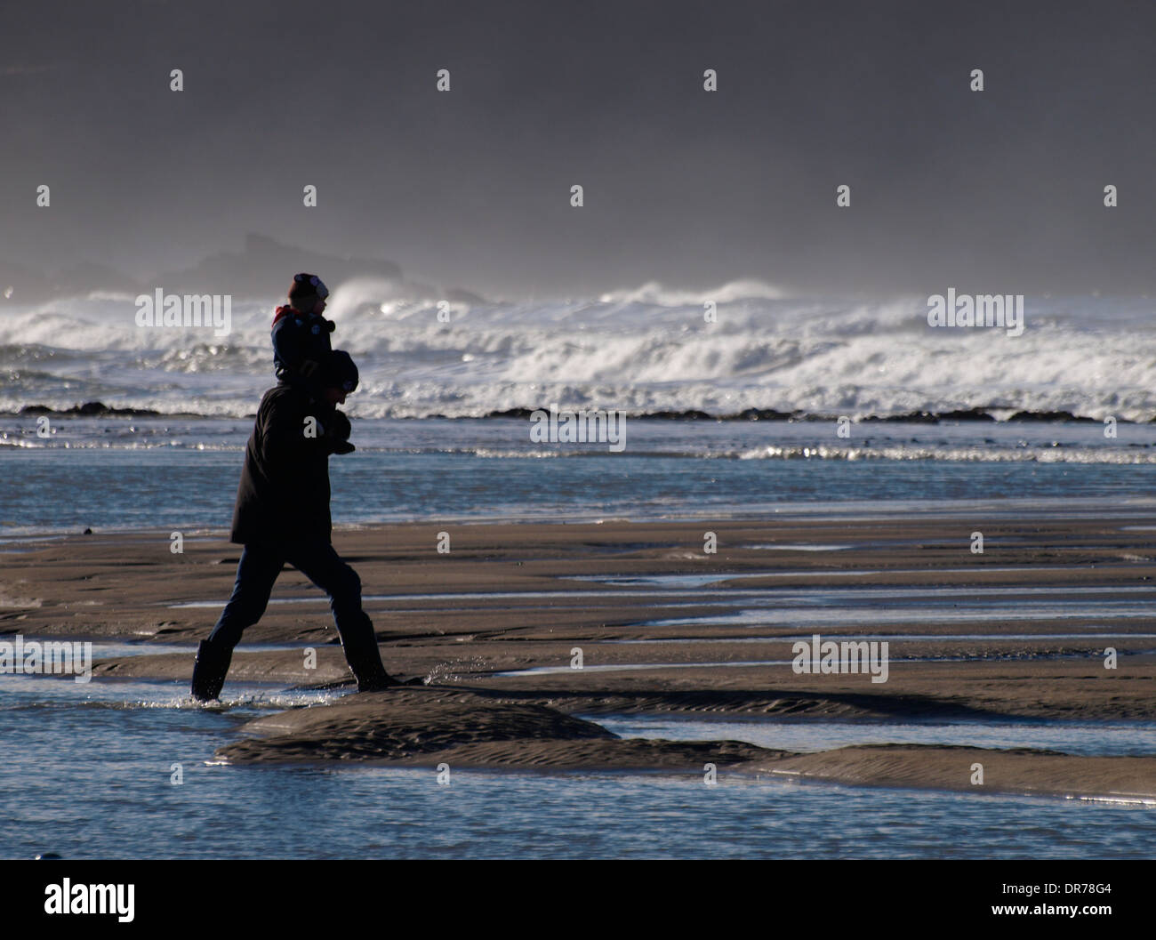 Mann mit Kind auf seinen Schultern, zu Fuß entlang des Strandes in Winter, Widemouth Bay, Cornwall, Großbritannien Stockfoto