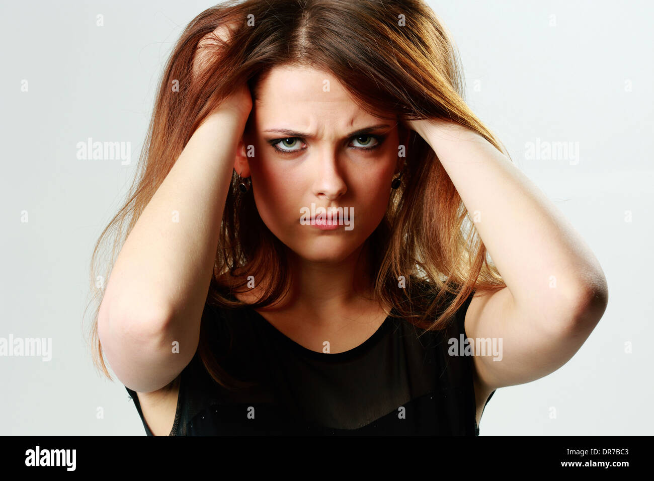 Böse Mädchen berühren den Kopf auf grauem Hintergrund Stockfoto