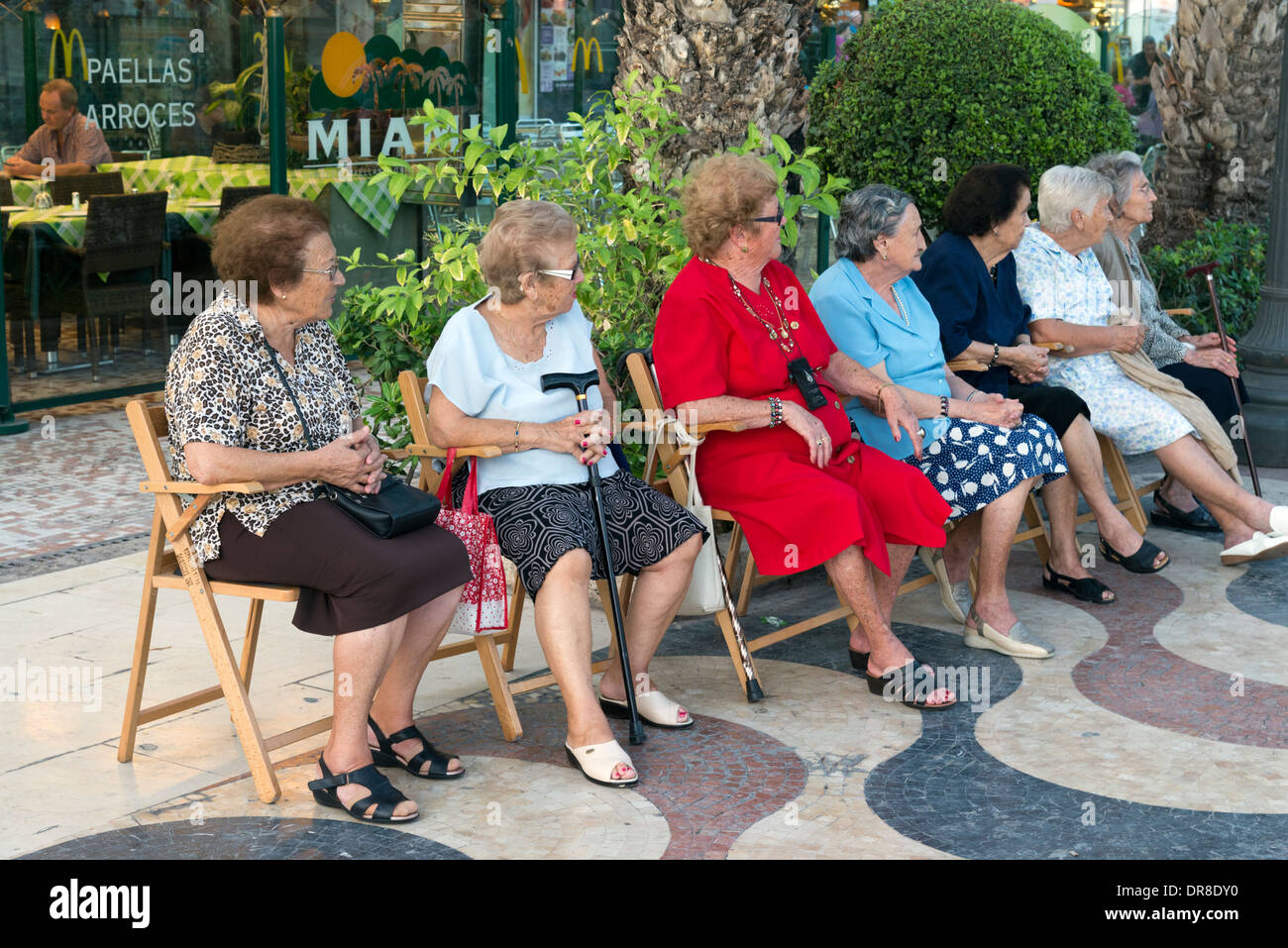Ältere Frauen sitzen auf hölzernen Stühlen auf der Paseo-Explanada de Espana, Alicante, Costa Blanca, Spanien Stockfoto