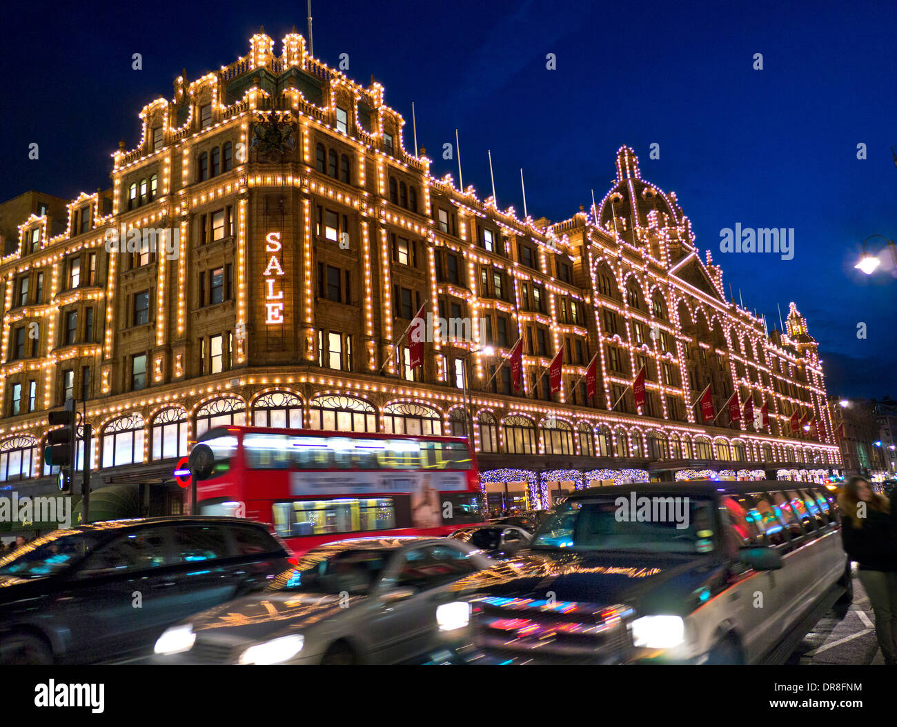 Das Kaufhaus Harrods in der Abenddämmerung mit beleuchteten "Sale" Schild Shopper rot Bus vorbei Taxis & Stretch-Limousine Knightsbridge London SW1 Stockfoto