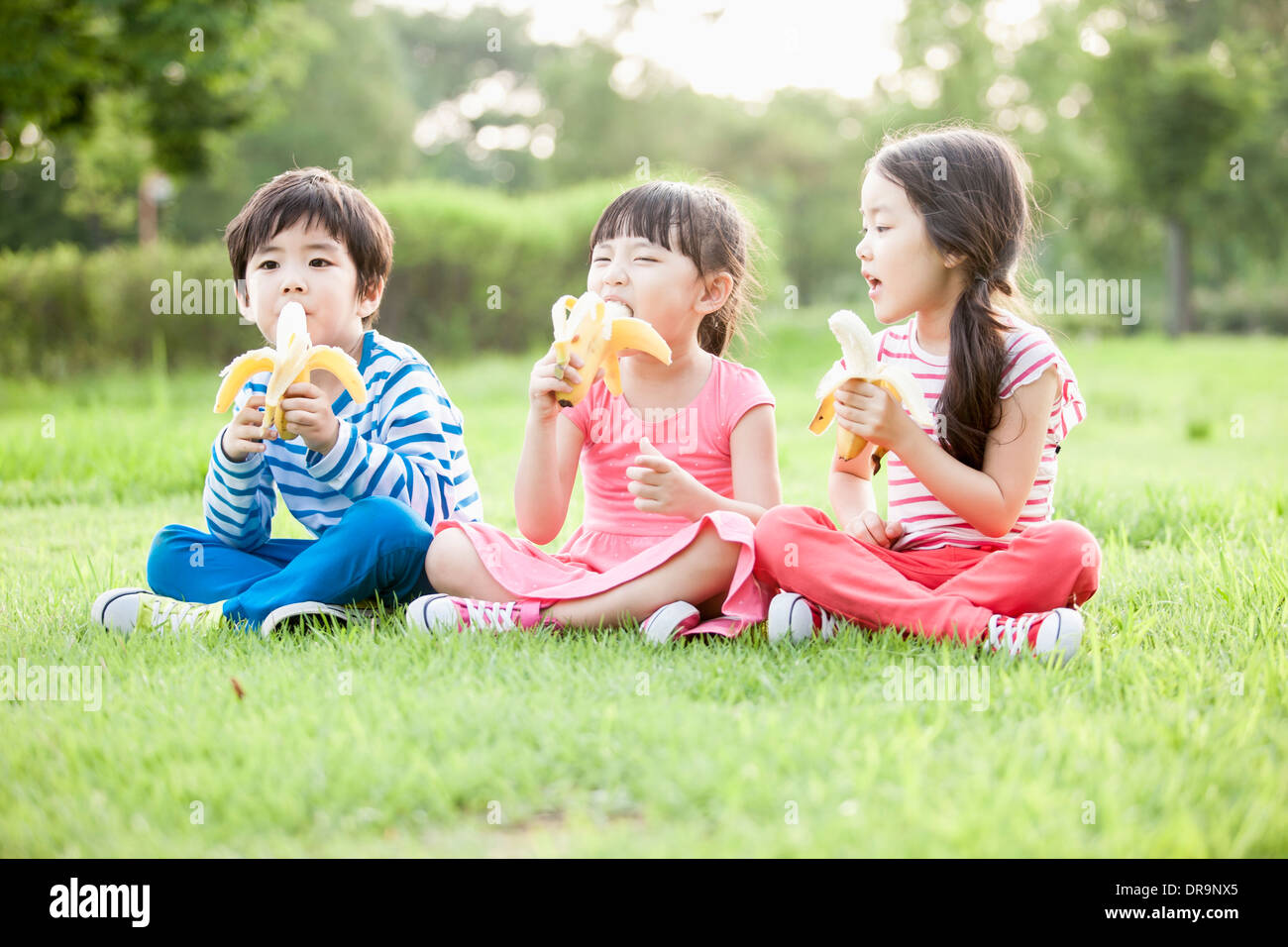 Kinder sitzen auf dem Rasen Bananen essen Stockfoto