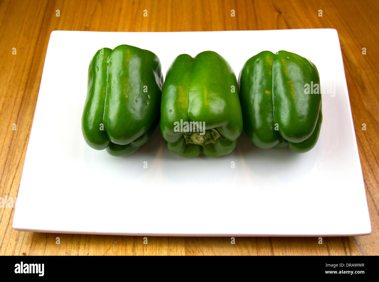 3 grüne Paprika auf einem weißen Teller auf einer hölzernen Theke Stockfoto