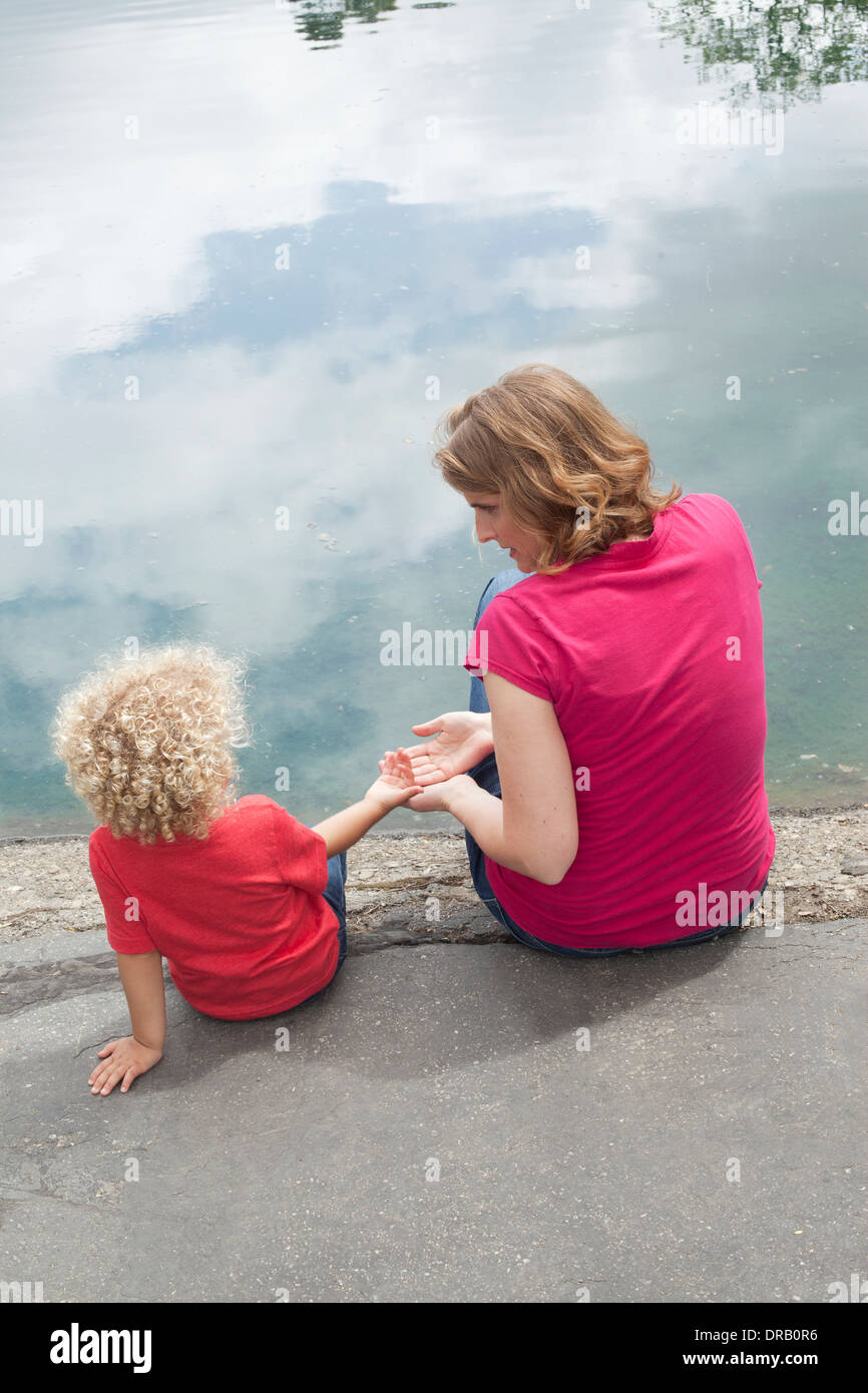 Rückansicht des kleinen Jungen an der Mutter Hand am Flussufer Stockfoto