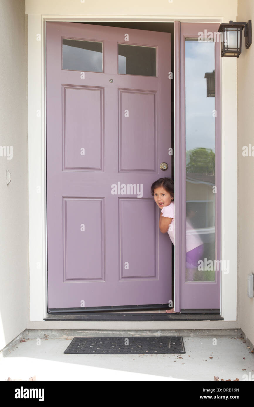 Überrascht, kleines Mädchen mit offener Tür am Eingang des Hauses Stockfoto