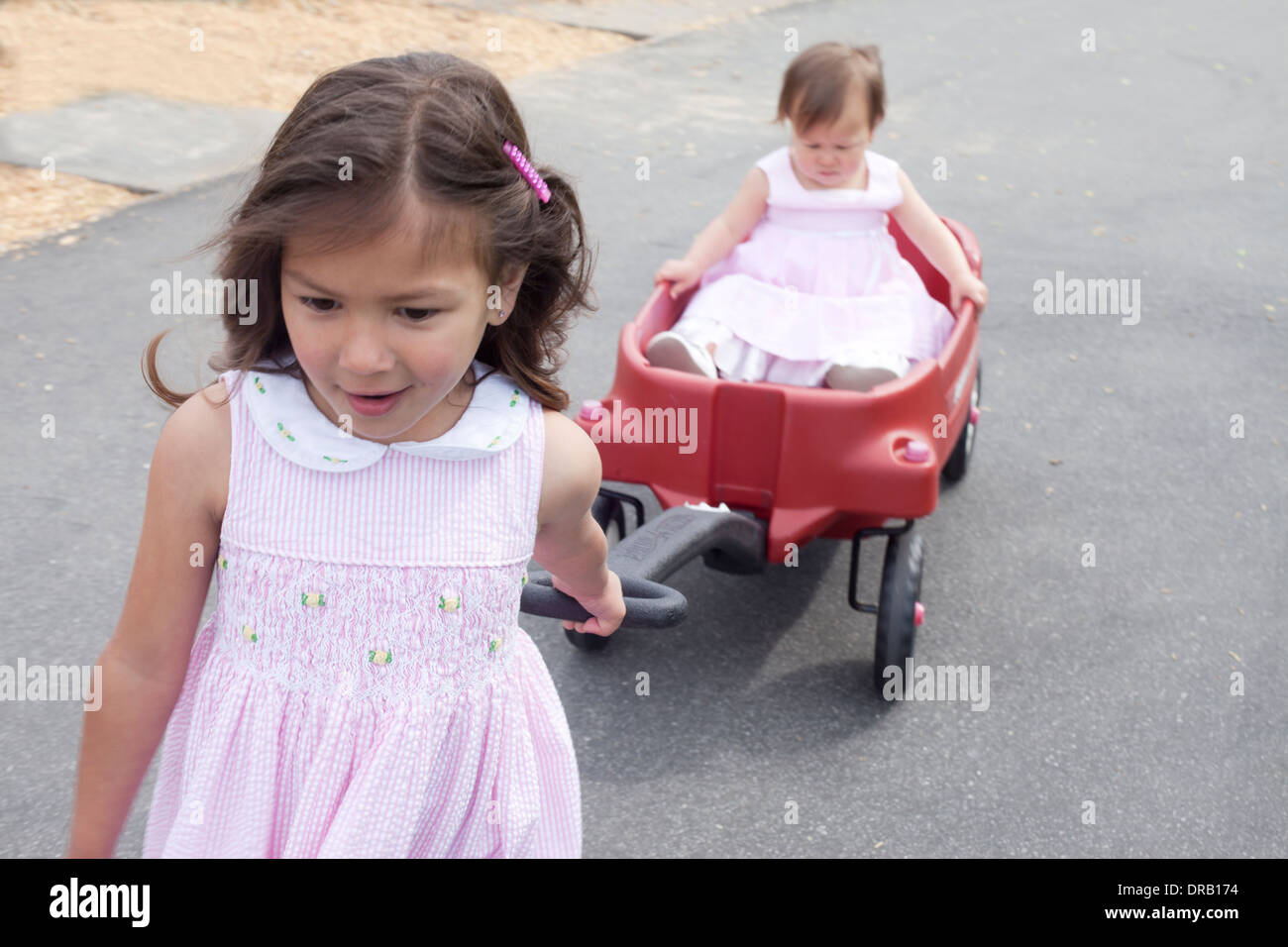 Ältere Schwester ziehen ihre jüngere Schwester in einem roten Wagen Stockfoto