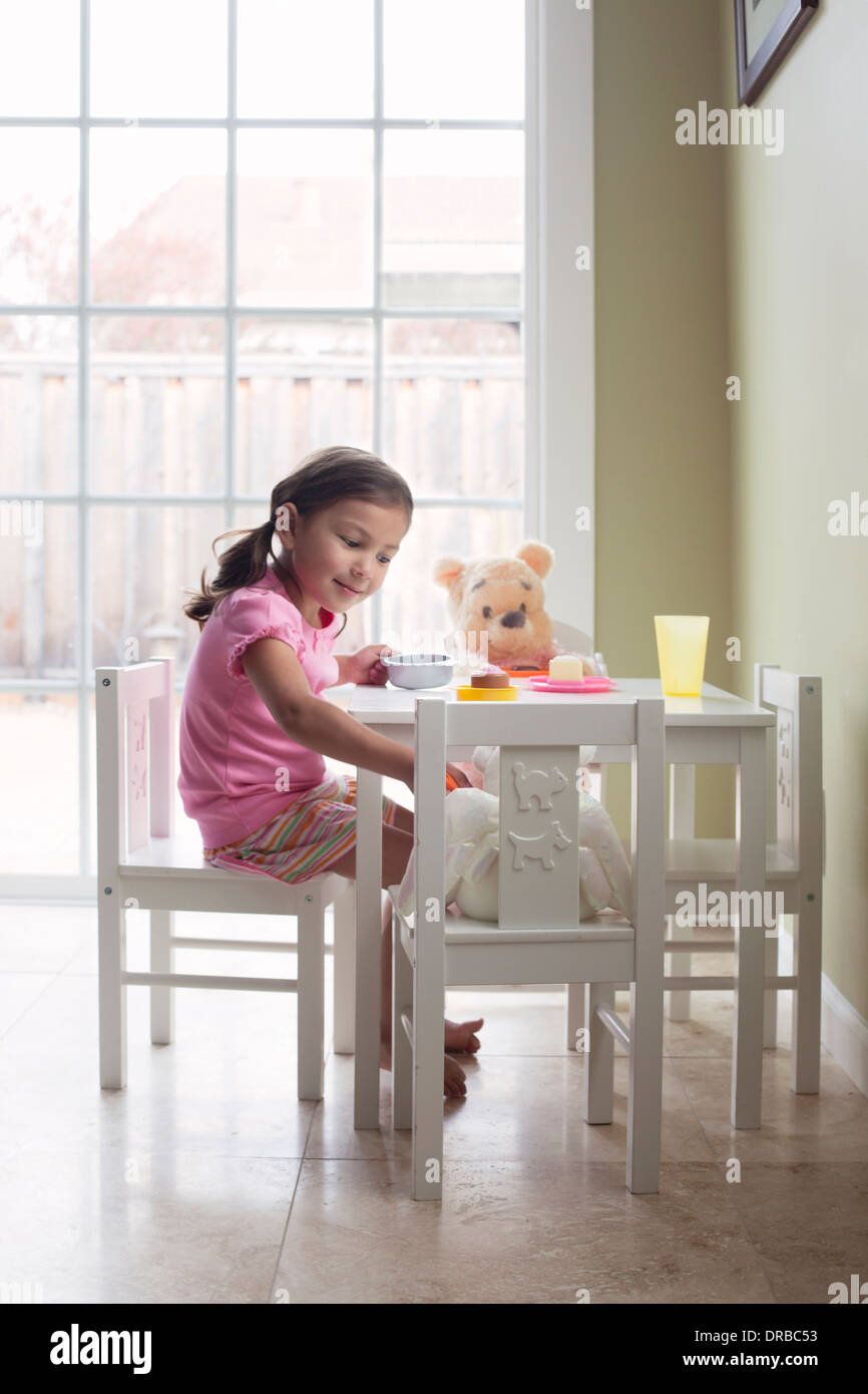 Glückliche kleine Mädchen Fütterung Teddybär am Esstisch Stockfoto