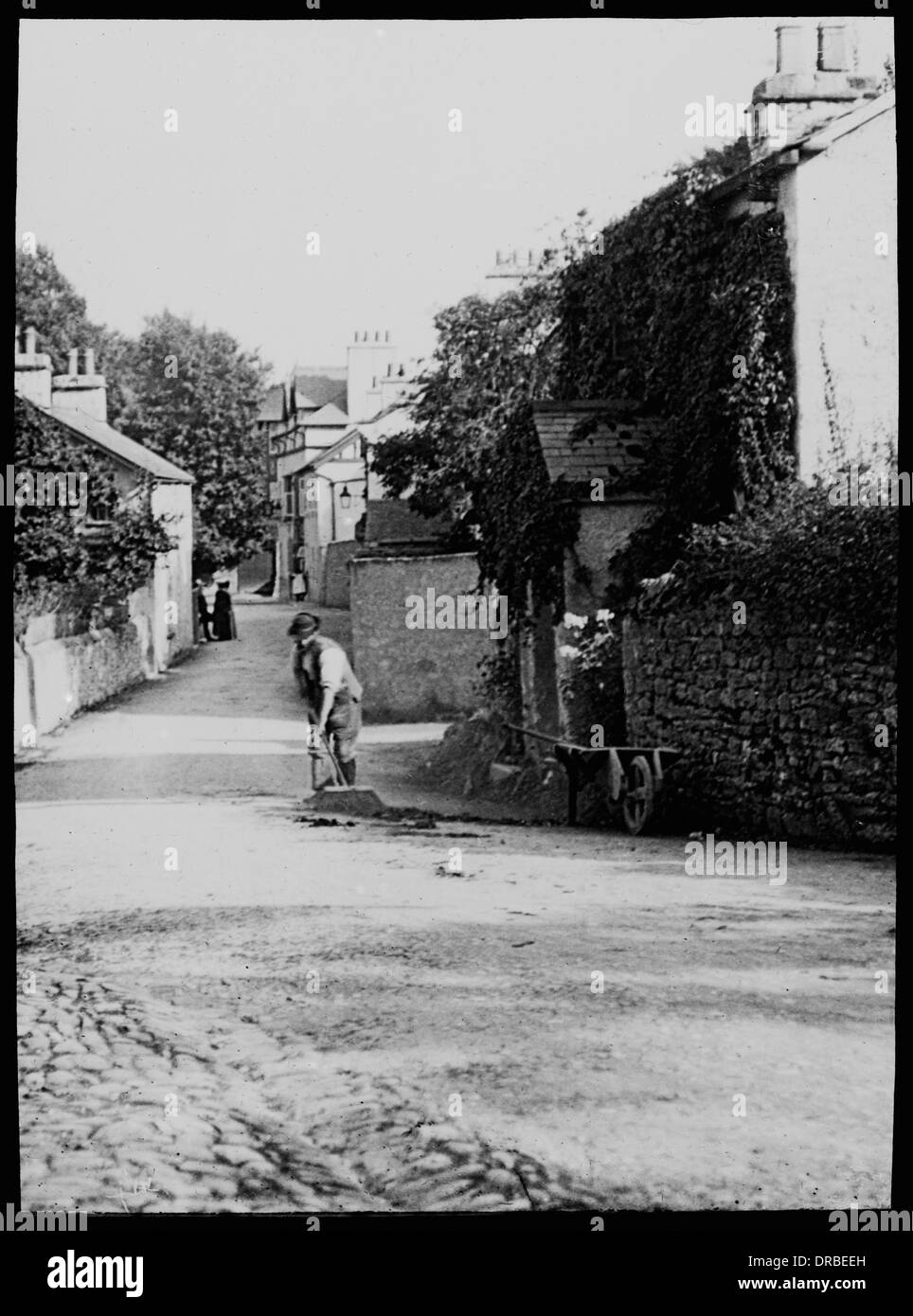 Straßenszene, Beetham, Cumbria (dann Westmorland), Lake District, England, im Jahre 1906. Mann die Straße fegen. Übernommen aus einem Objektträger Laterne. Stockfoto