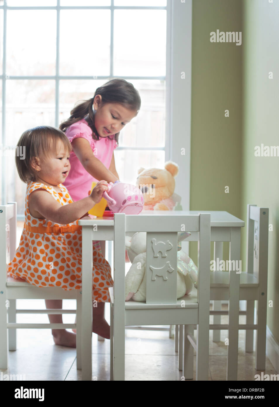 Niedliche kleine Mädchen mit Spielzeug Wasserkocher und Teddybär am Esstisch Stockfoto