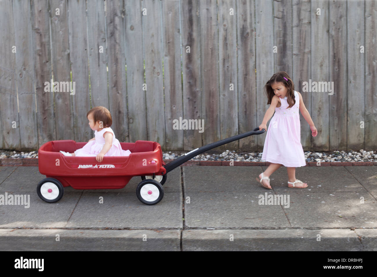 Ältere Schwester ihrer jüngeren Schwester in einem roten Wagen ziehen. Stockfoto