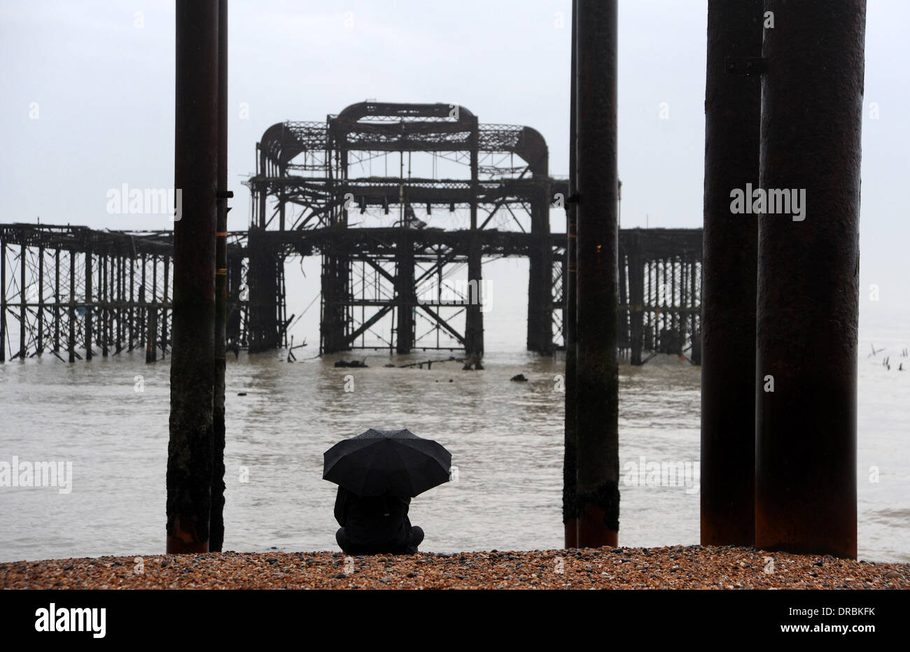 Eine Person sitzt unter einem Regenschirm Ausblick auf das Meer von der West Pier in Brighton Beach im Nieselregen und frühen Morgennebel UK Stockfoto