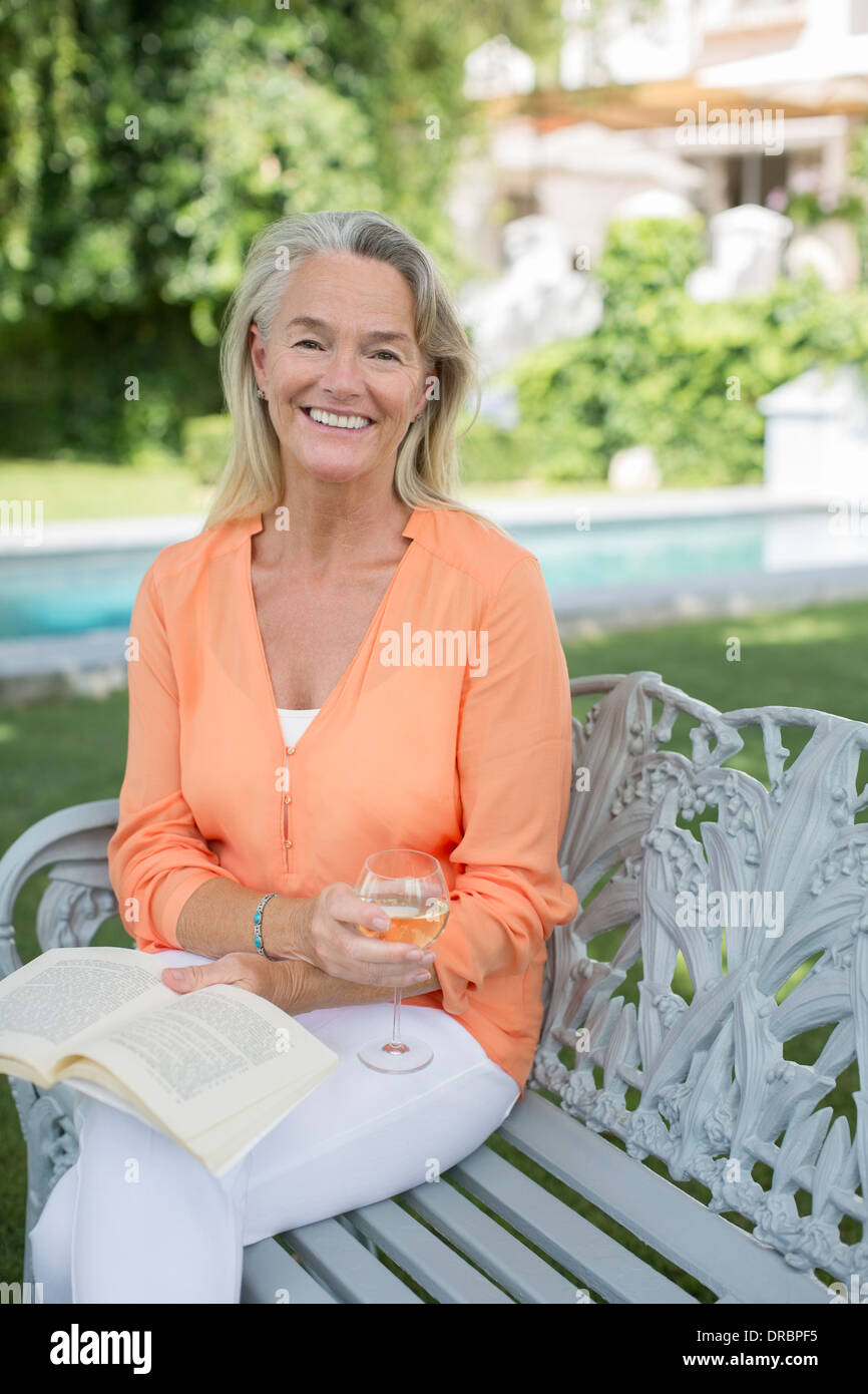 Lächelnde senior Frau Buch lesen und Weintrinken im Hinterhof Stockfoto