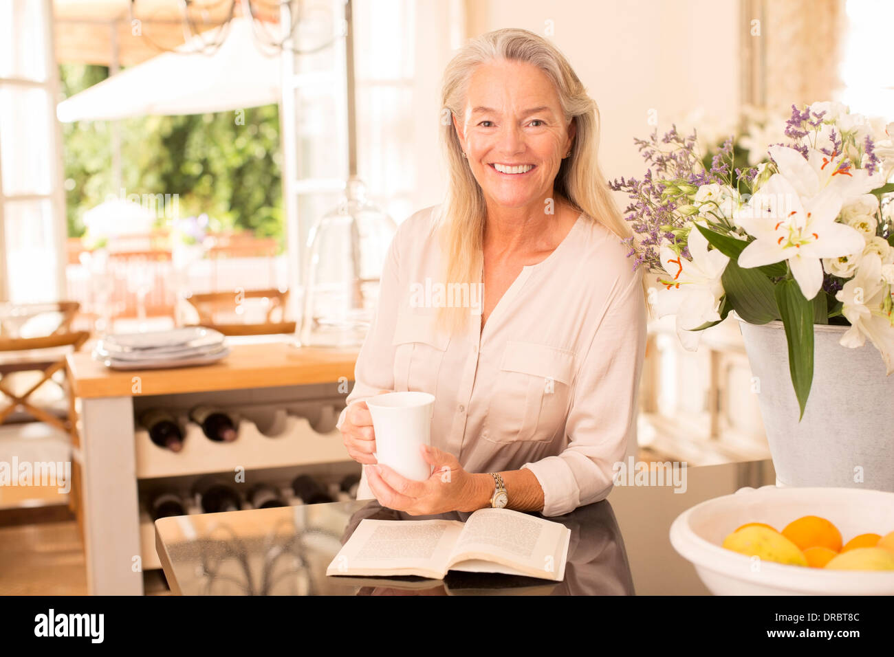 Ältere Frau Kaffee trinken und Buch in Küche Stockfoto