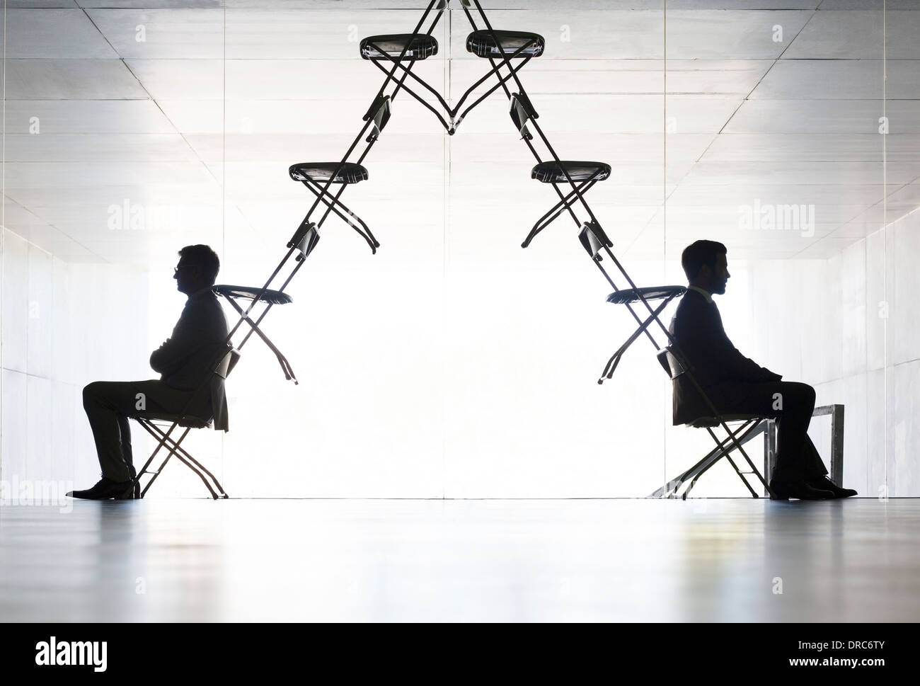 Geschäftsleute, die an den entgegengesetzten Enden der Installationskunst Büro Stuhl sitzen Stockfoto
