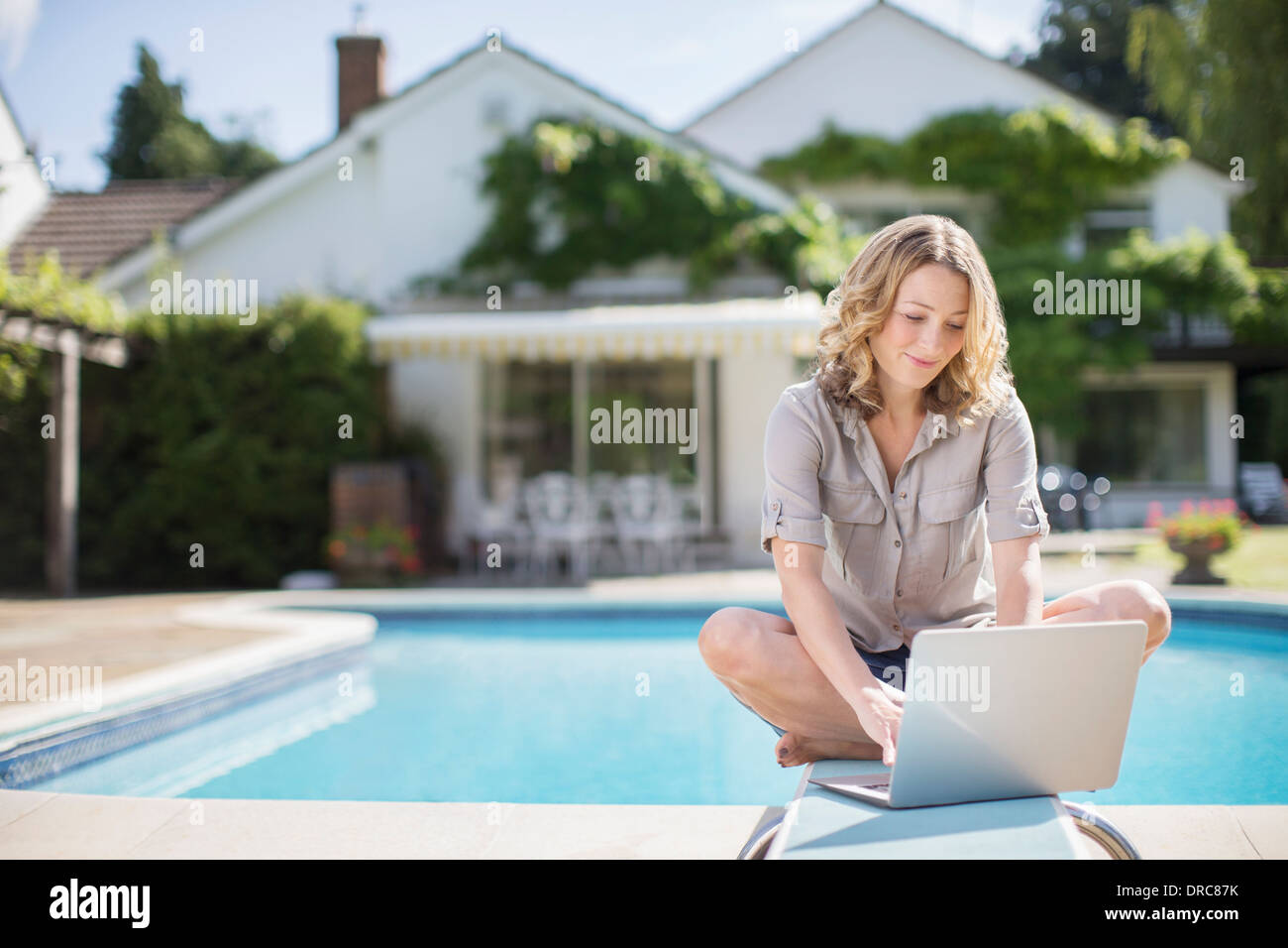 Frau mit Laptop auf Sprungbrett am Pool Stockfoto